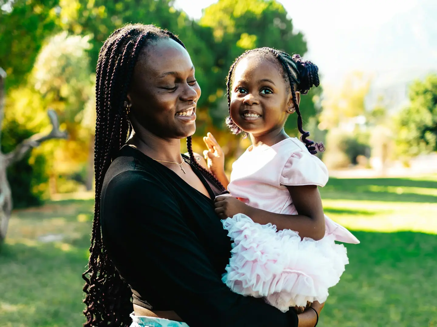 A mother holding her young daughter in a sunny park